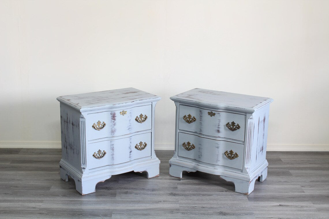 Pair of Mid-Century Painted nightstands with brass hardware.  The nightstands have been professionally refinished in a light gray tone in a distressed finish, with original brass hardware.  Dimensions; 26" Width x 16" Depth x 25" Height. 