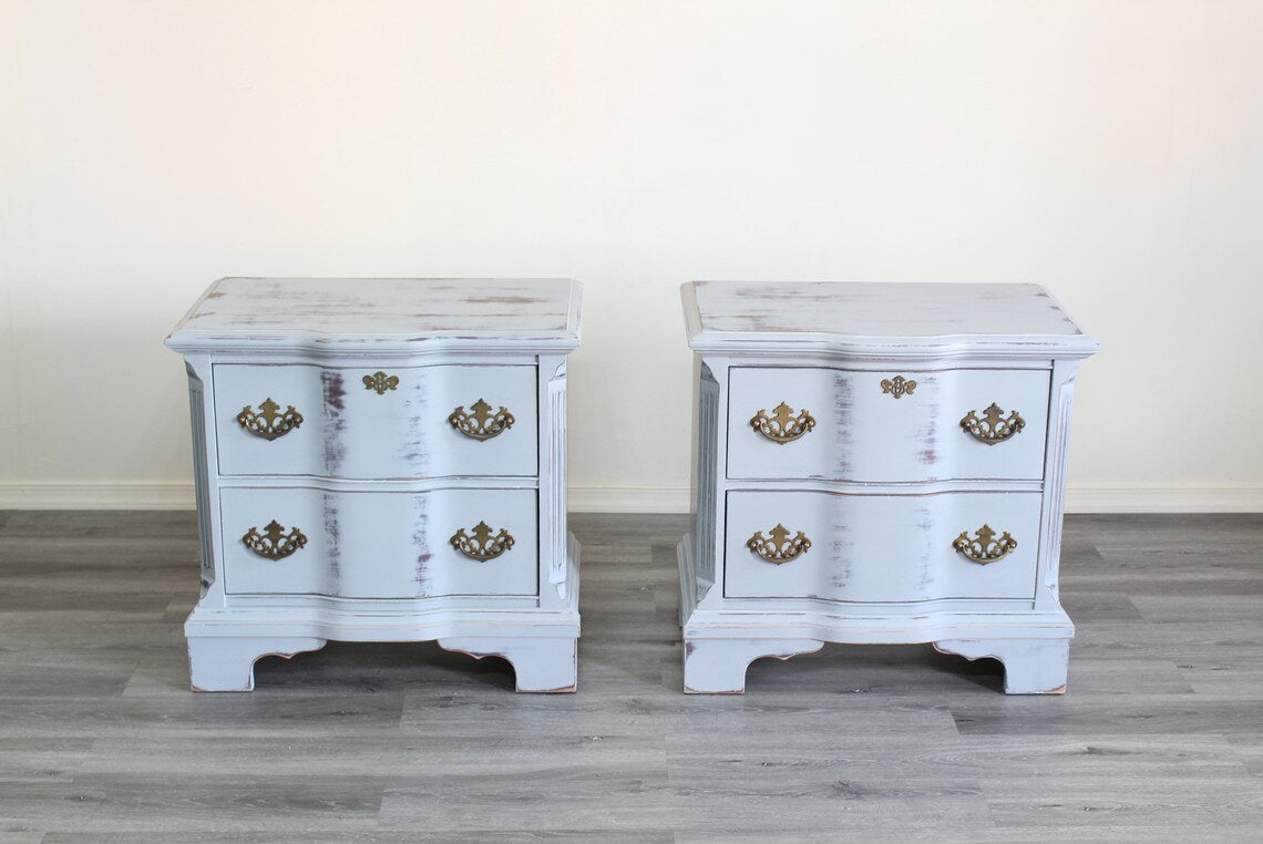 Pair of Mid-Century Painted nightstands with brass hardware.  The nightstands have been professionally refinished in a light gray tone in a distressed finish, with original brass hardware.  Dimensions; 26" Width x 16" Depth x 25" Height. 