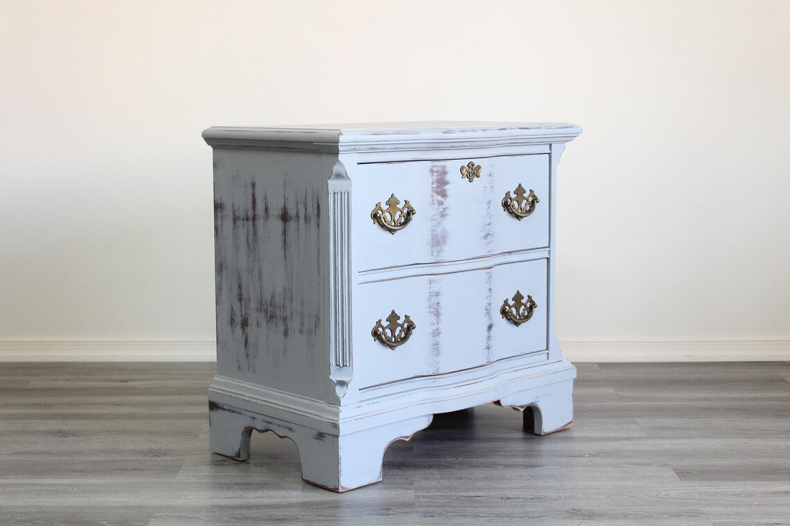 Pair of Mid-Century Painted nightstands with brass hardware.  The nightstands have been professionally refinished in a light gray tone in a distressed finish, with original brass hardware.  Dimensions; 26" Width x 16" Depth x 25" Height. 