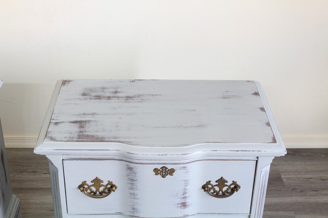 Pair of Mid-Century Painted nightstands with brass hardware.  The nightstands have been professionally refinished in a light gray tone in a distressed finish, with original brass hardware.  Dimensions; 26" Width x 16" Depth x 25" Height. 