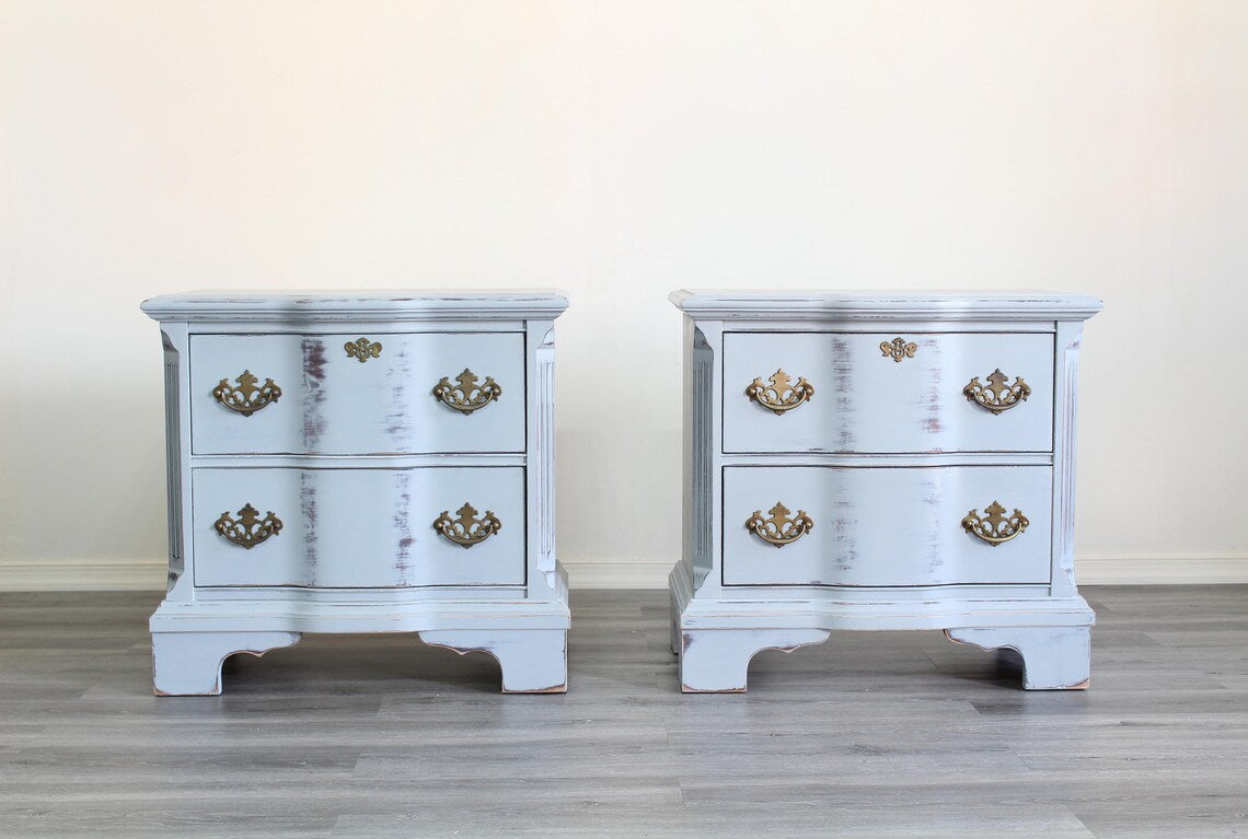 Pair of Mid-Century Painted nightstands with brass hardware.  The nightstands have been professionally refinished in a light gray tone in a distressed finish, with original brass hardware.  Dimensions; 26" Width x 16" Depth x 25" Height. 