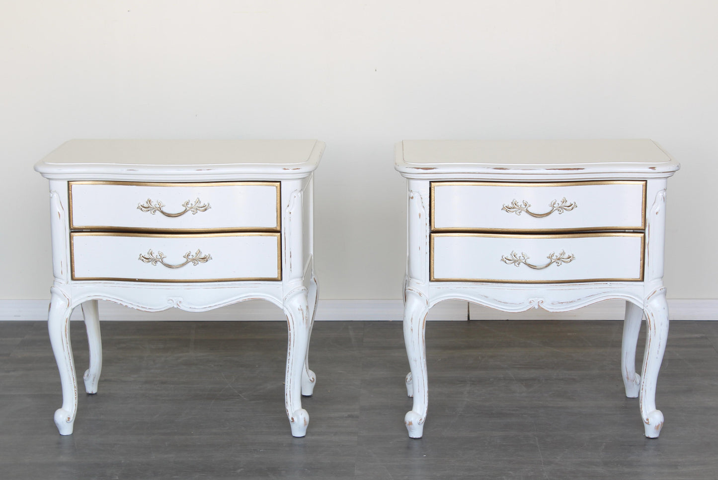 Vintage pair of French provincial nightstands of two drawers.  The nightstands are solid built with dovetail joints, are professionally refinished in white with a distressed finish and gold painted accents.  Dimensions: 24.5"Width x 16"Depth x 24"Height.