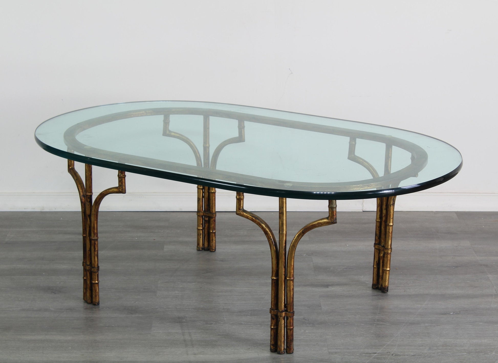 Vintage Hollywood Regency faux bamboo metal coffee table with glass top.  This is a gilt metal oval coffee table with glass top.  Dimensions; 46" Width x 26" Depth x 17" Height. 